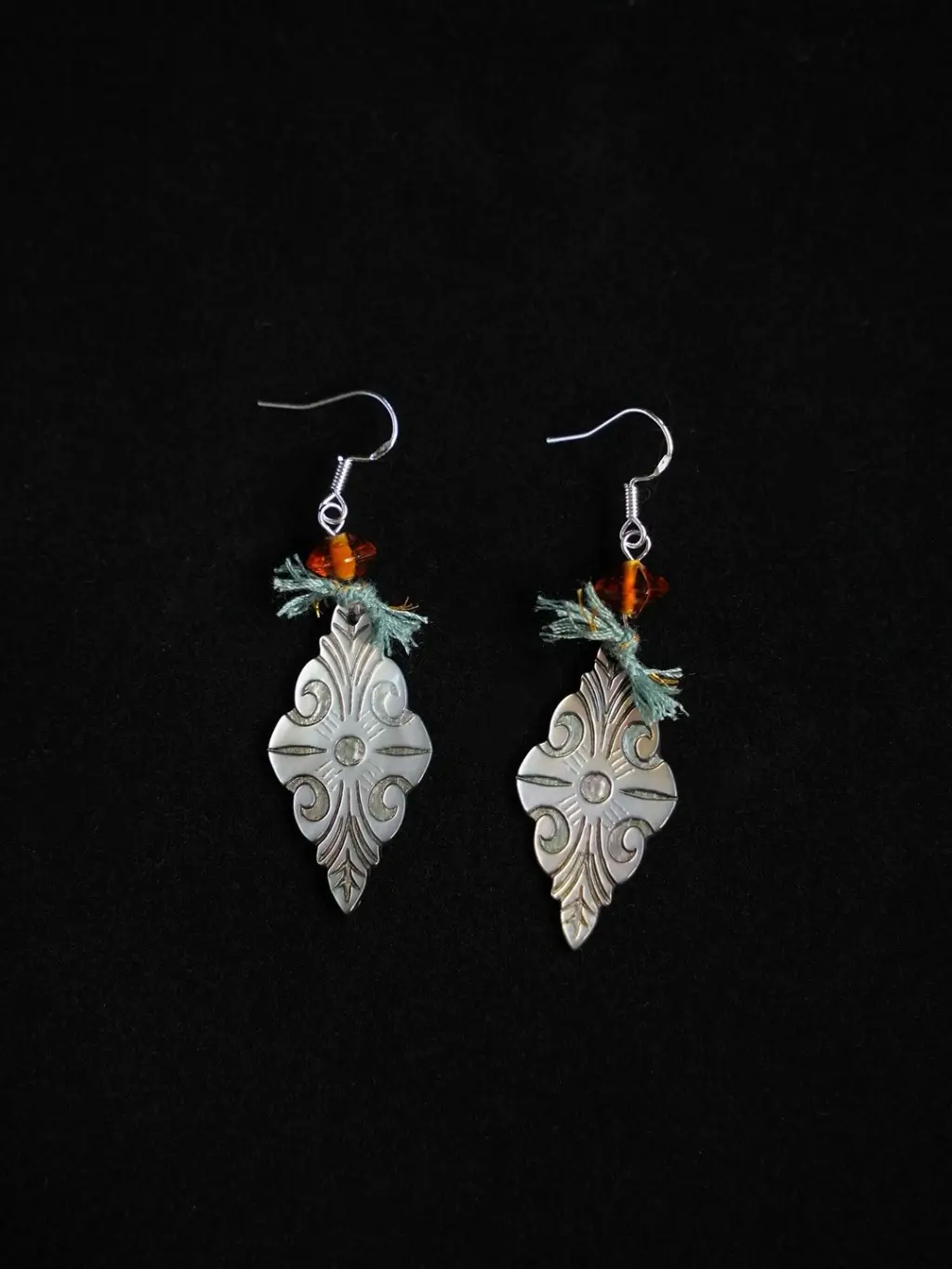 A pair of Fanta-orange glass earrings standing out against a solid black background.