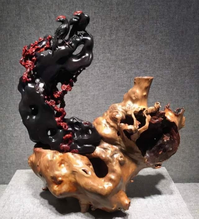 An intricate Guilin Blood-Red Jasper carving of magpies on plum blossoms, set on a wood base.