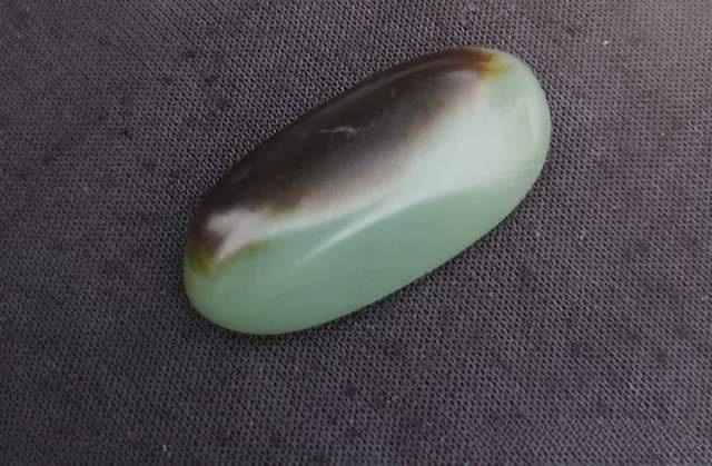 A smooth, oval-shaped Hetian jade stone from Guangxi with a pale green body and a dark brown top.