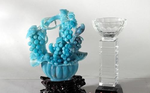 An intricate blue-green Guicui quartzite carving of a grape basket next to a crystal trophy.
