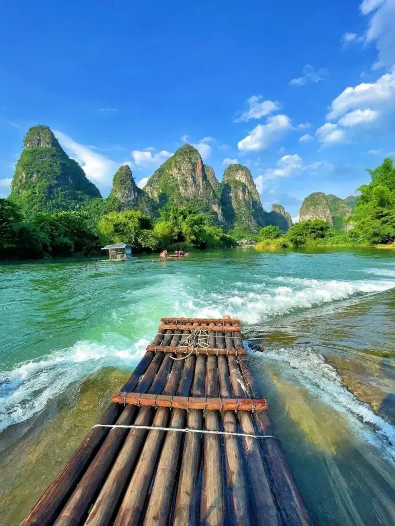 A traditional bamboo raft glides down a turquoise river surrounded by steep karst mountains in Guilin.