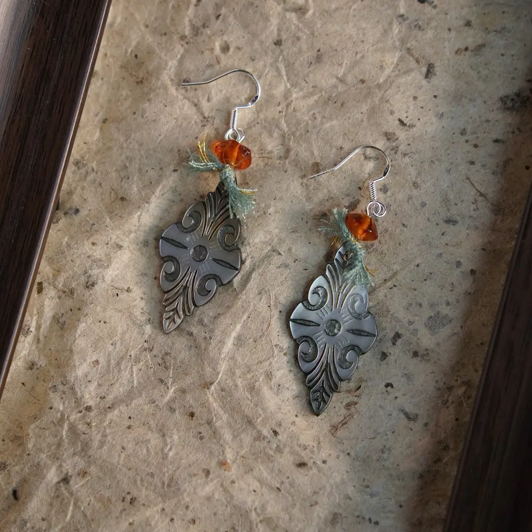Hand-knotted midnight teal cotton cord earrings laid on distressed, mottled paper.