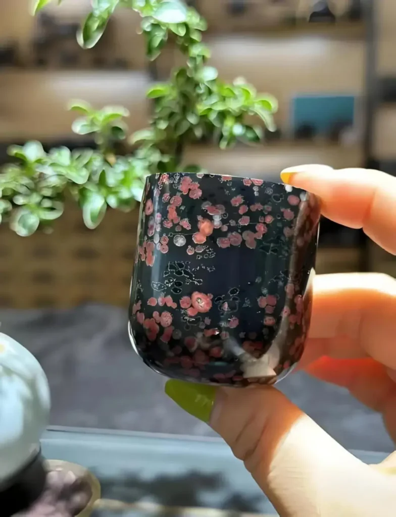 Polished Henan Plum Blossom Jade tea cup with distinct red floral patterns on a black base.