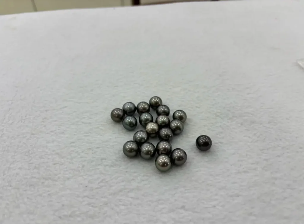 A small cluster of round, dark grey Hepu pearls with high metallic luster on a white surface.