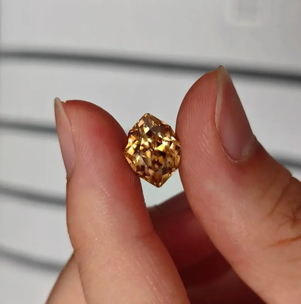 A hand holding a faceted yellow-brown cassiterite showing high clarity and intense light refraction.