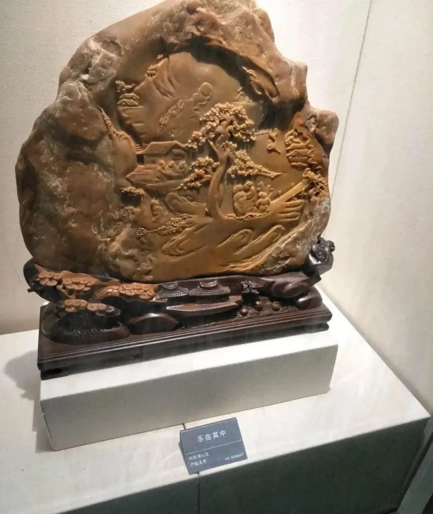 A large Huangshan jade carving depicting a traditional Chinese landscape on a wooden stand.