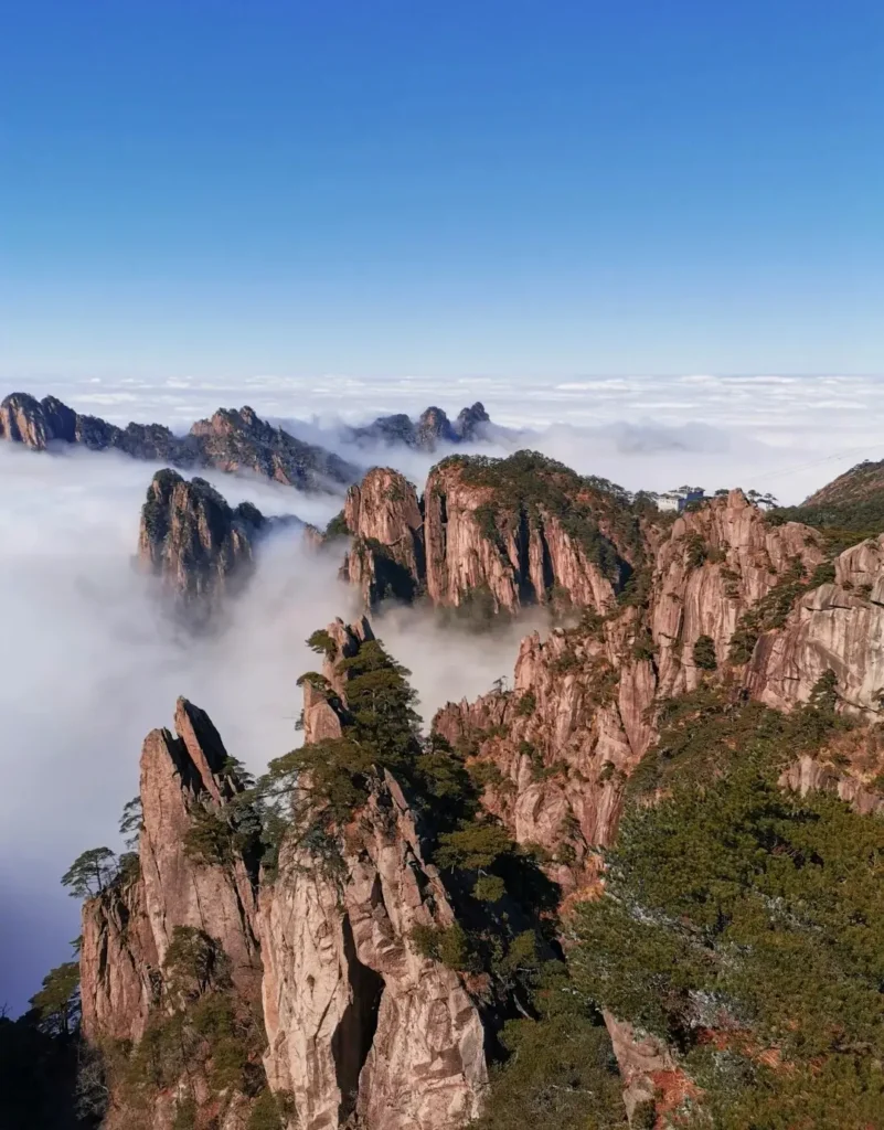 Aerial view of jagged granite peaks in Anhui Huangshan rising above a thick sea of white clouds.