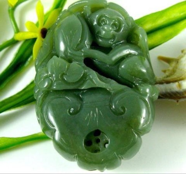 A monkey holding a peach carved from green Jilin serpentine jade near yellow flowers.