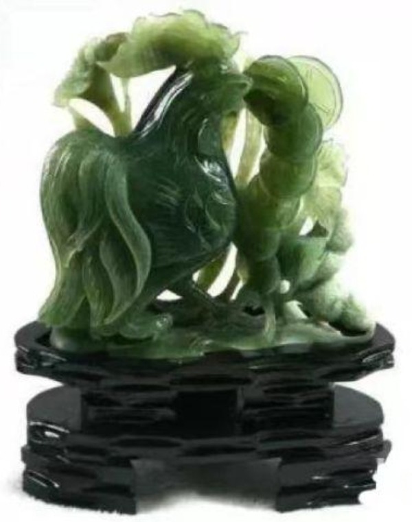 A rooster and coins sculpture carved from green Jilin serpentine jade on a dark stand.