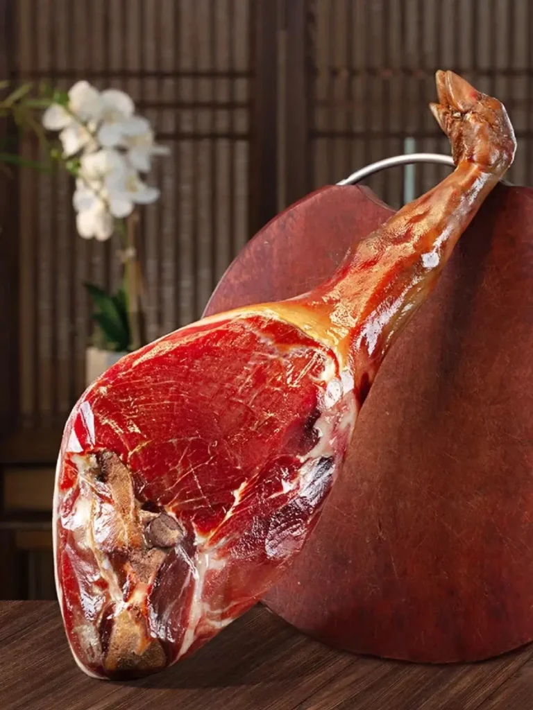 A whole cured Zhejiang Jinhua ham with a deep red cut surface rests on a wooden stand.