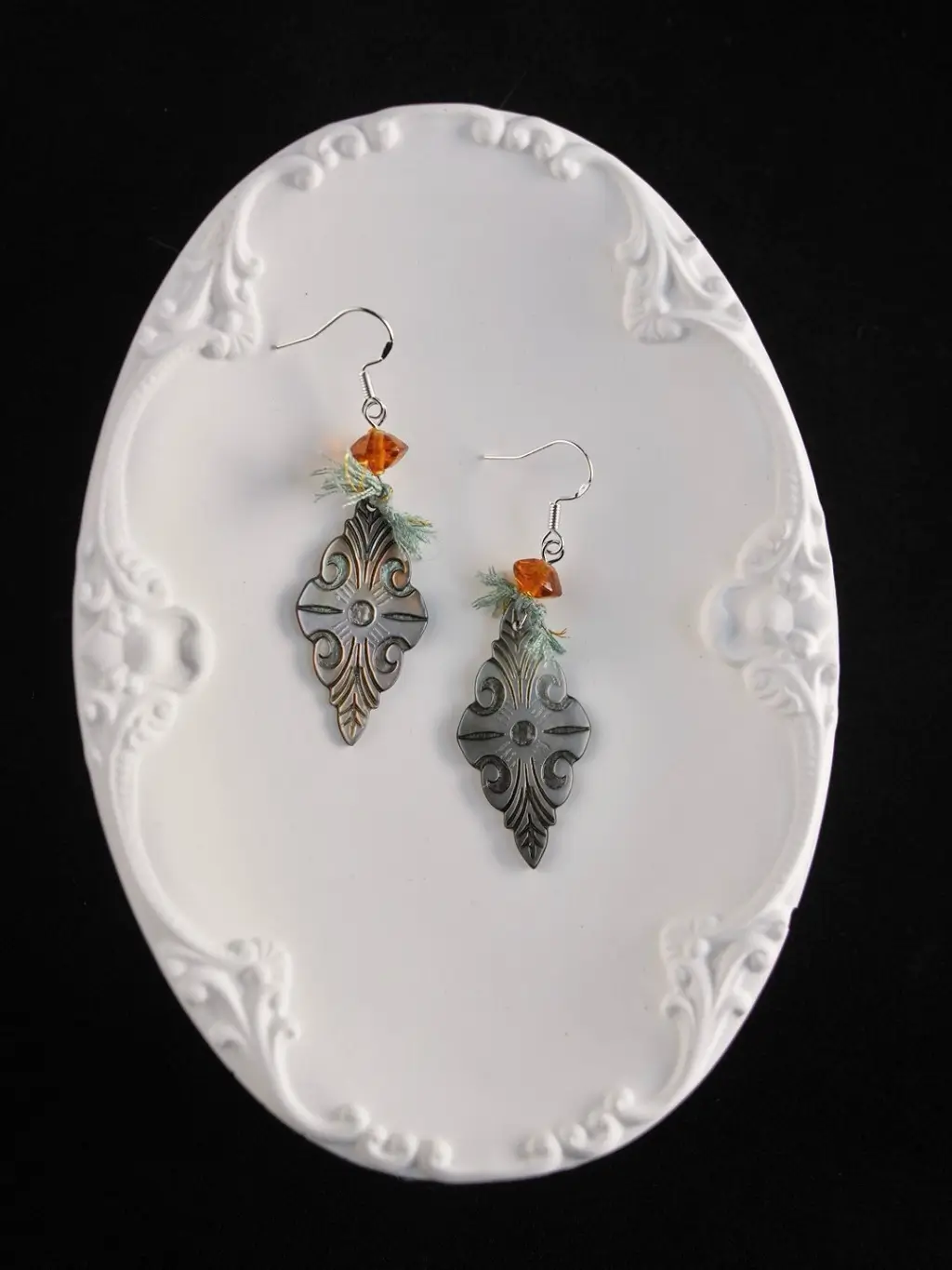 A pair of hand-knotted cord earrings on a white porcelain plate, detailing the artisanal weave.