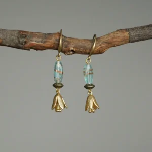 Lily of the Valley drop earrings hanging on a rustic wooden branch against a gray background.