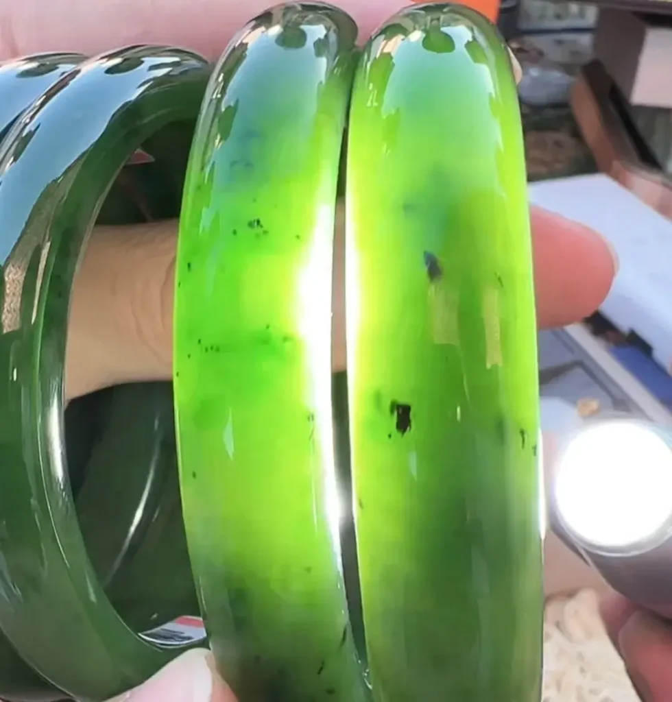 Translucent vibrant green Xinjiang Manas jasper bangles showing natural dark chromite spots under light.