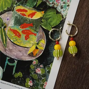 Top-down view of an open art book featuring Henri Matisse’s Goldfish (1912), alongside handmade glass bead hoop earrings inspired by Fauvist color and form.