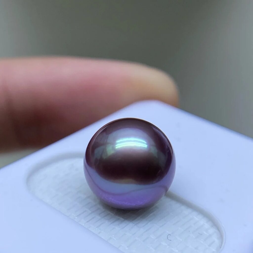A highly saturated metallic purple Edison pearl with intense mirror-like luster resting on a white base.
