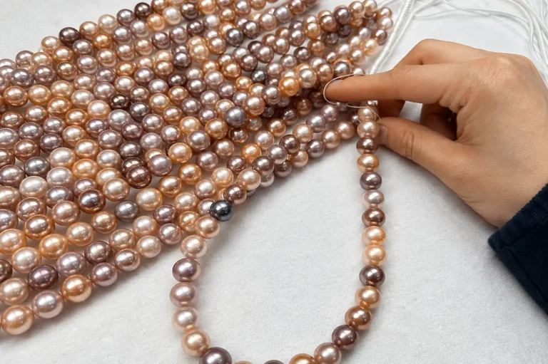 A hand matching and selecting round multicolor Edison pearl strands on a white workbench.