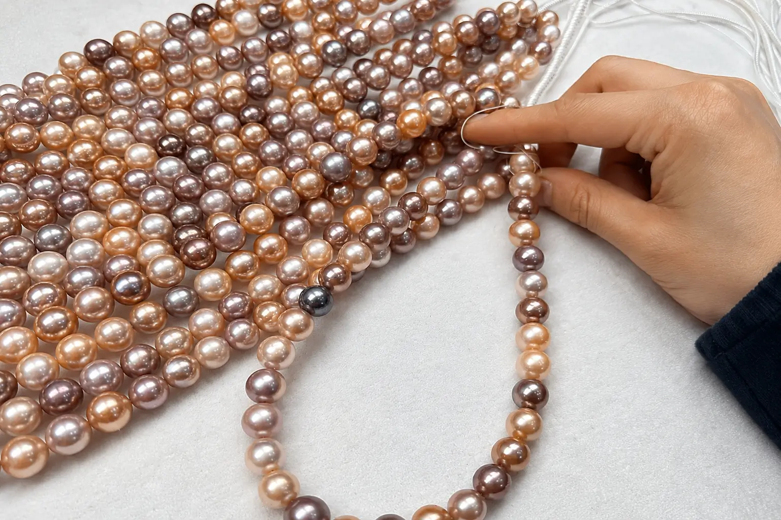 A hand matching and selecting round multicolor Edison pearl strands on a white workbench.