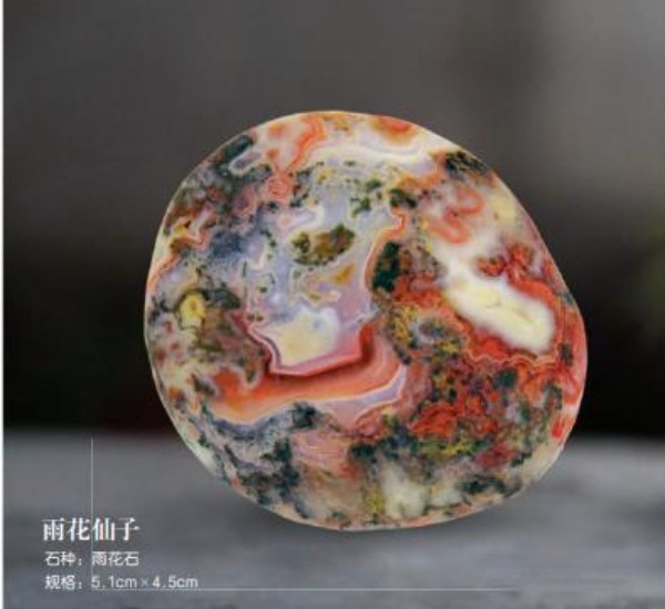 A polished Yuhua agate stone named "Rain Flower Fairy" with intricate red, white, and green patterns.
