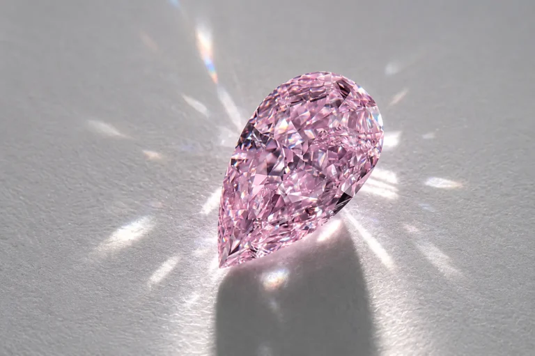 A pear-cut purple diamond reflecting brilliant light rays on a light gray surface.