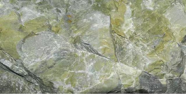A close-up of a yellowish-green and grey Panlong jade rough mineral deposit.