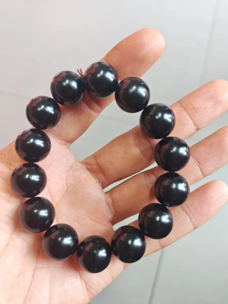 A hand holding a polished Fushun jet stone bracelet featuring large, glossy black spherical beads.