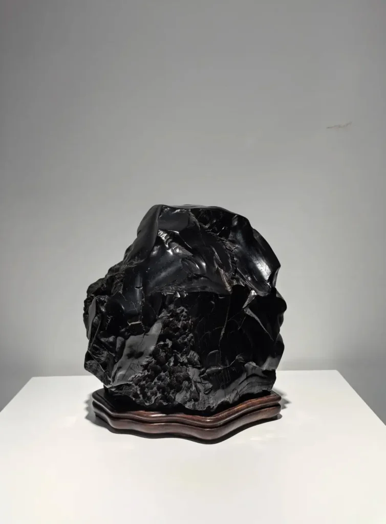 A large, naturally shaped polished black jet stone displayed on a wooden base.