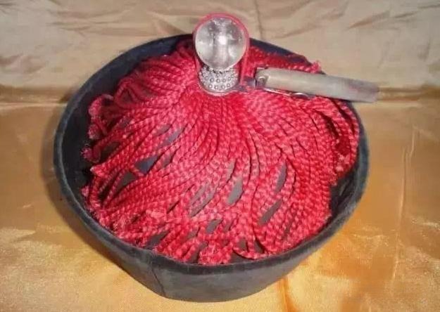 A clear crystal top bead mounted on a traditional Qing Dynasty official's hat with red tassels.