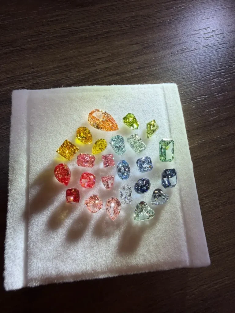 A collection of multi-colored diamonds arranged on a white velvet pad, casting long shadows.