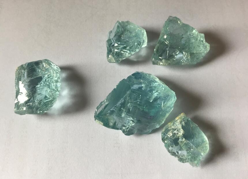 Five rough, icy-blue aquamarine crystals showing natural prismatic mineral structures.