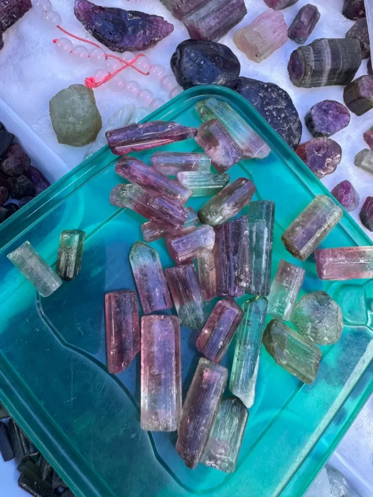 A pile of rough, multicolored tourmaline crystal prisms in a green tray at a Xinjiang market.