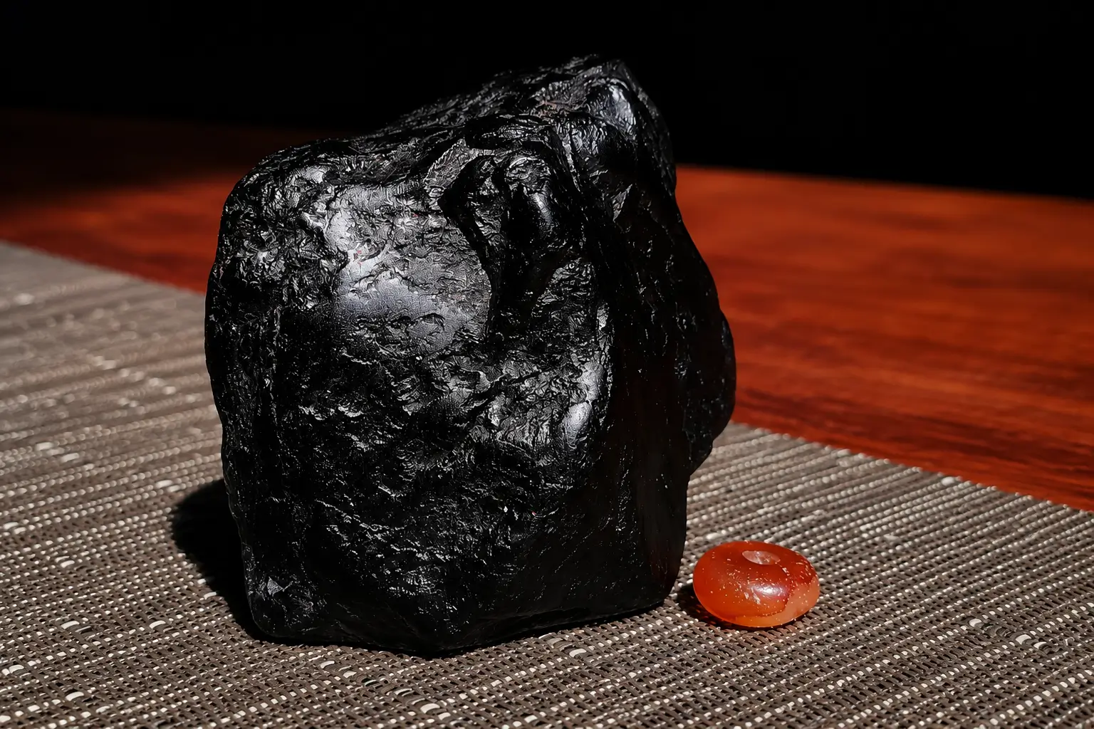 Large opaque black Shanxi jet stone with strong luster next to a vibrant orange amber bead.