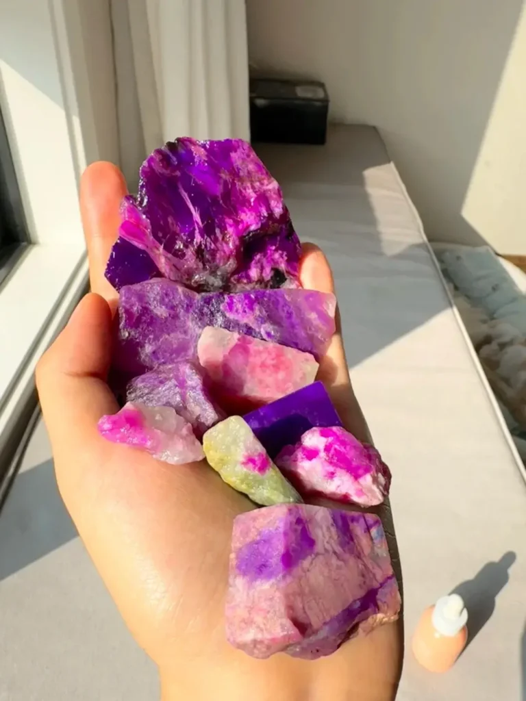 A handful of raw, unpolished mineral stones in vibrant shades of purple, magenta, pink, and green.