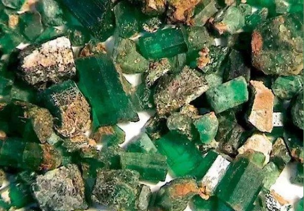 A cluster of rough, vibrant green Xinjiang emerald crystals embedded in natural rock matrix.