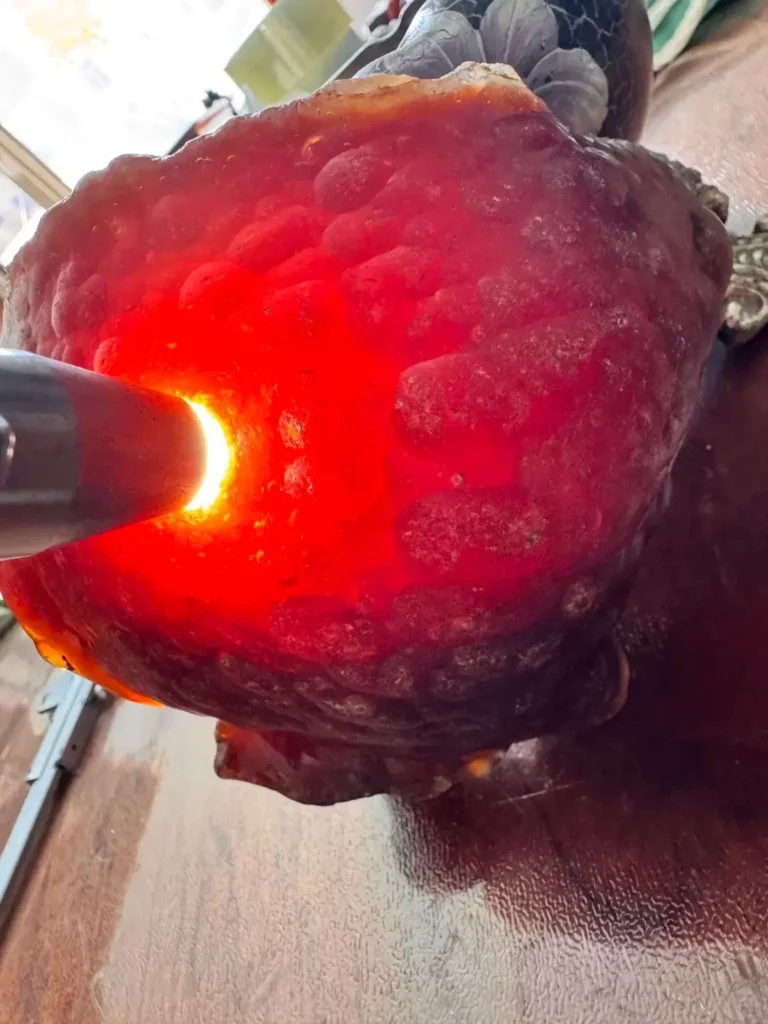 Flashlight illuminating the brilliant translucent red interior of a raw Xunke agate stone.