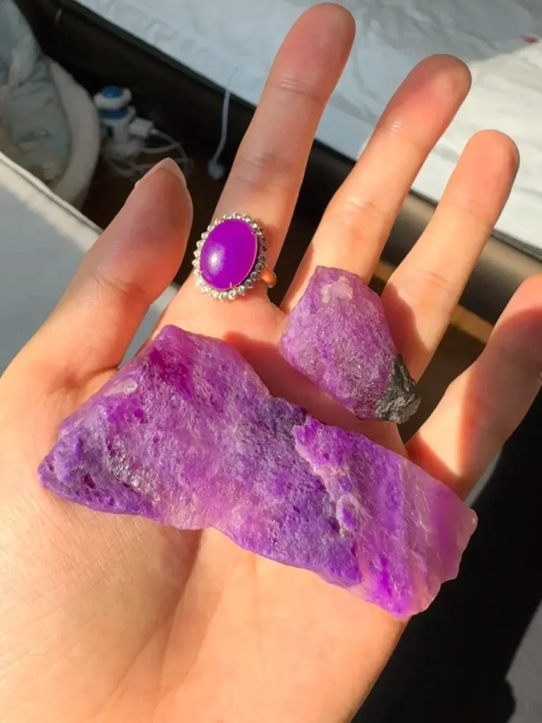 Polished purple gemstone ring contrasted against raw, rough mineral ores on a hand.