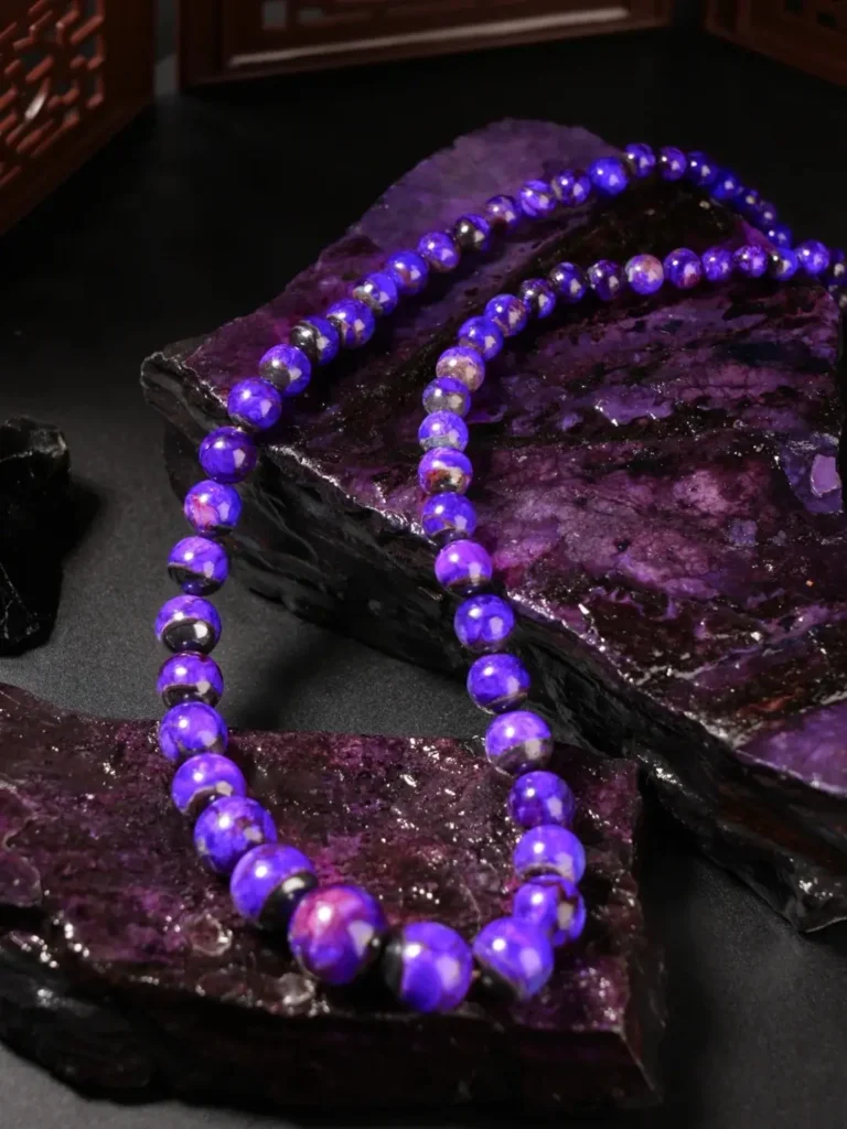 A royal purple Sugilite beaded necklace draped over large, raw dark violet mineral stones.