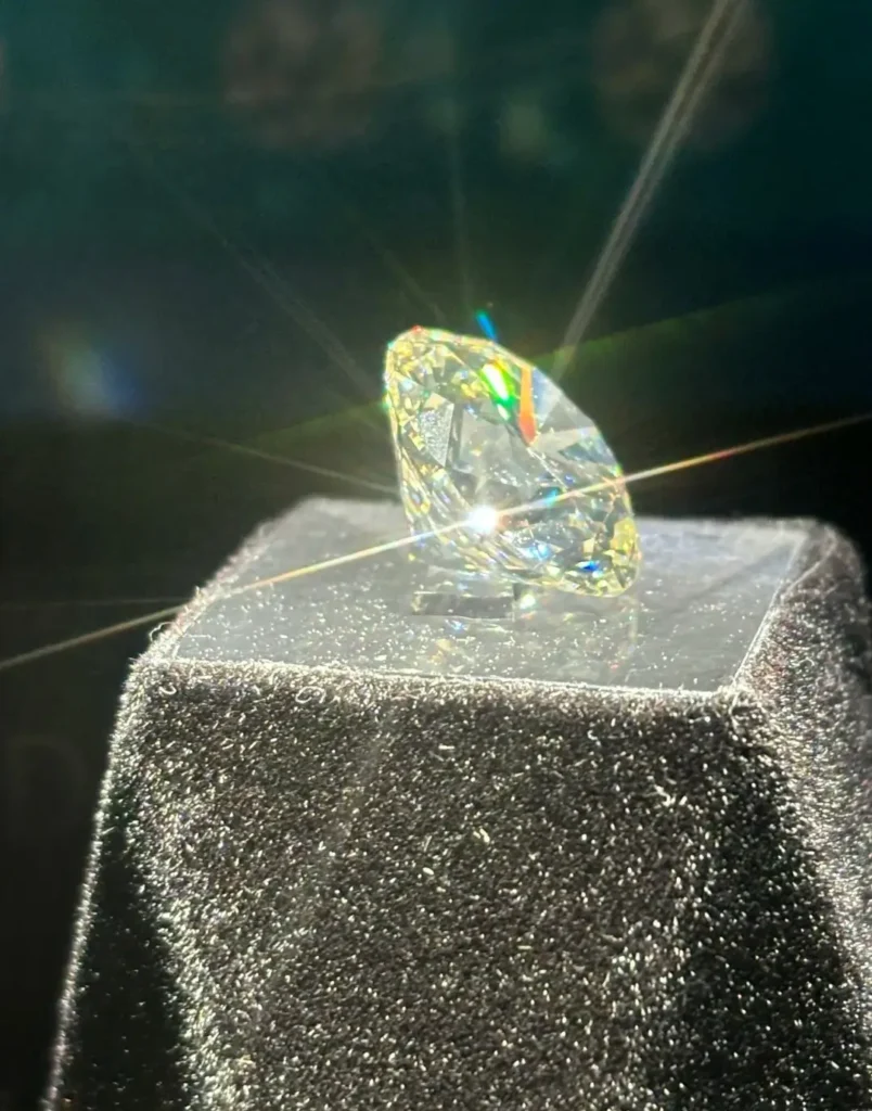A 12.50 carat diamond on a black stand showing vivid rainbow fire under a spotlight.