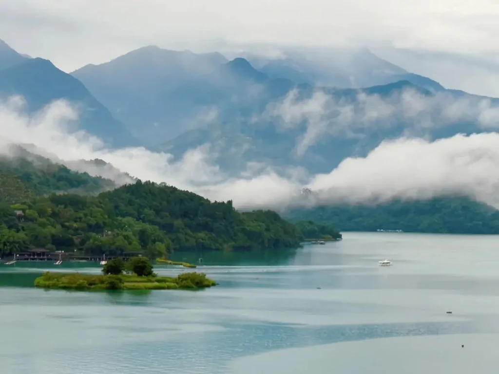 Misty view of Sun Moon Lake in Taiwan with lush green hills and fog-covered mountains after rain.