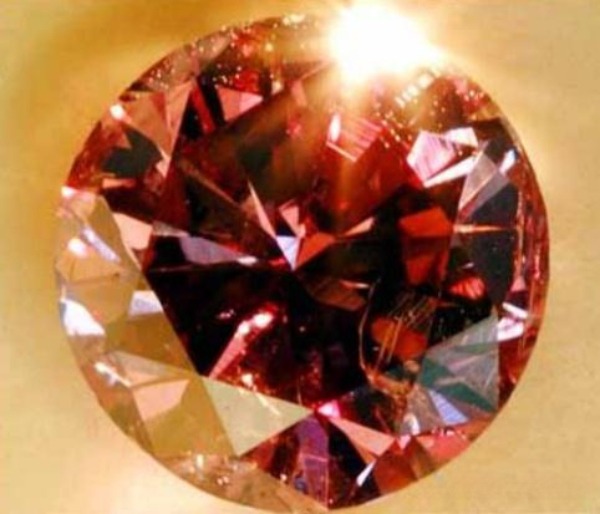 A round-cut diamond showing deep purple and purplish-red hues under a bright light source.