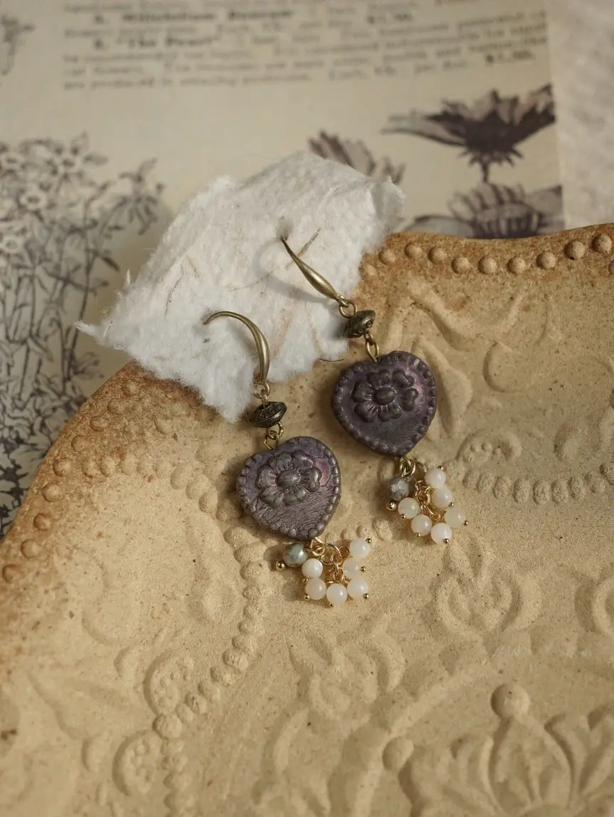 Detailed heart earrings on a textured plate with botanical illustration paper.
