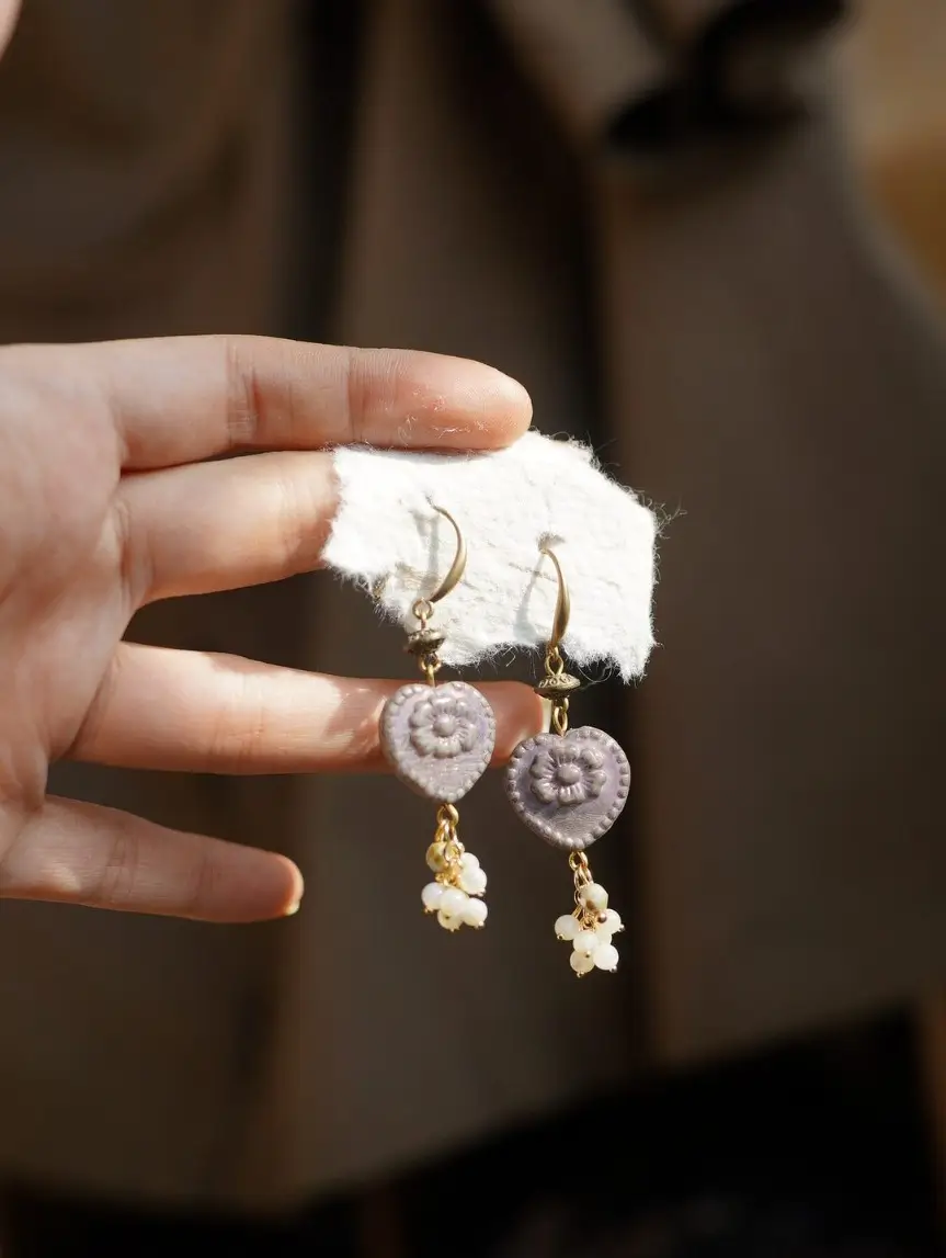 Hand holding heart earrings against a blurred brown background, showing scale.
