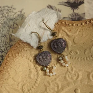 Victorian relief heart earrings with purple glass and shell pearl tassels on an antique plate.