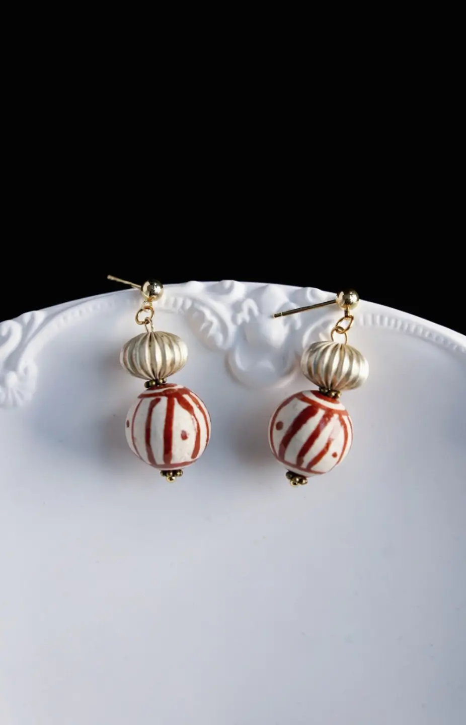 A pair of vintage earrings resting on a smooth white ceramic plate.