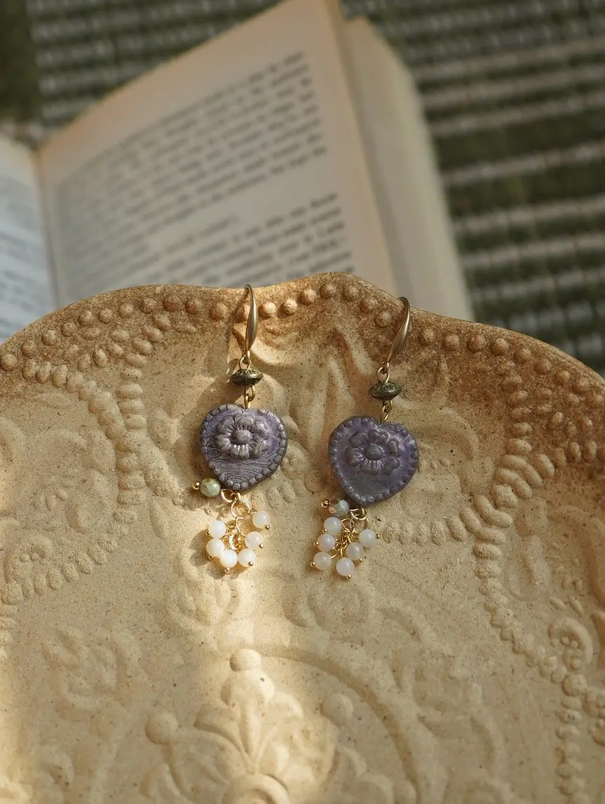 Purple relief heart earrings on a decorative ceramic plate with a vintage book behind.