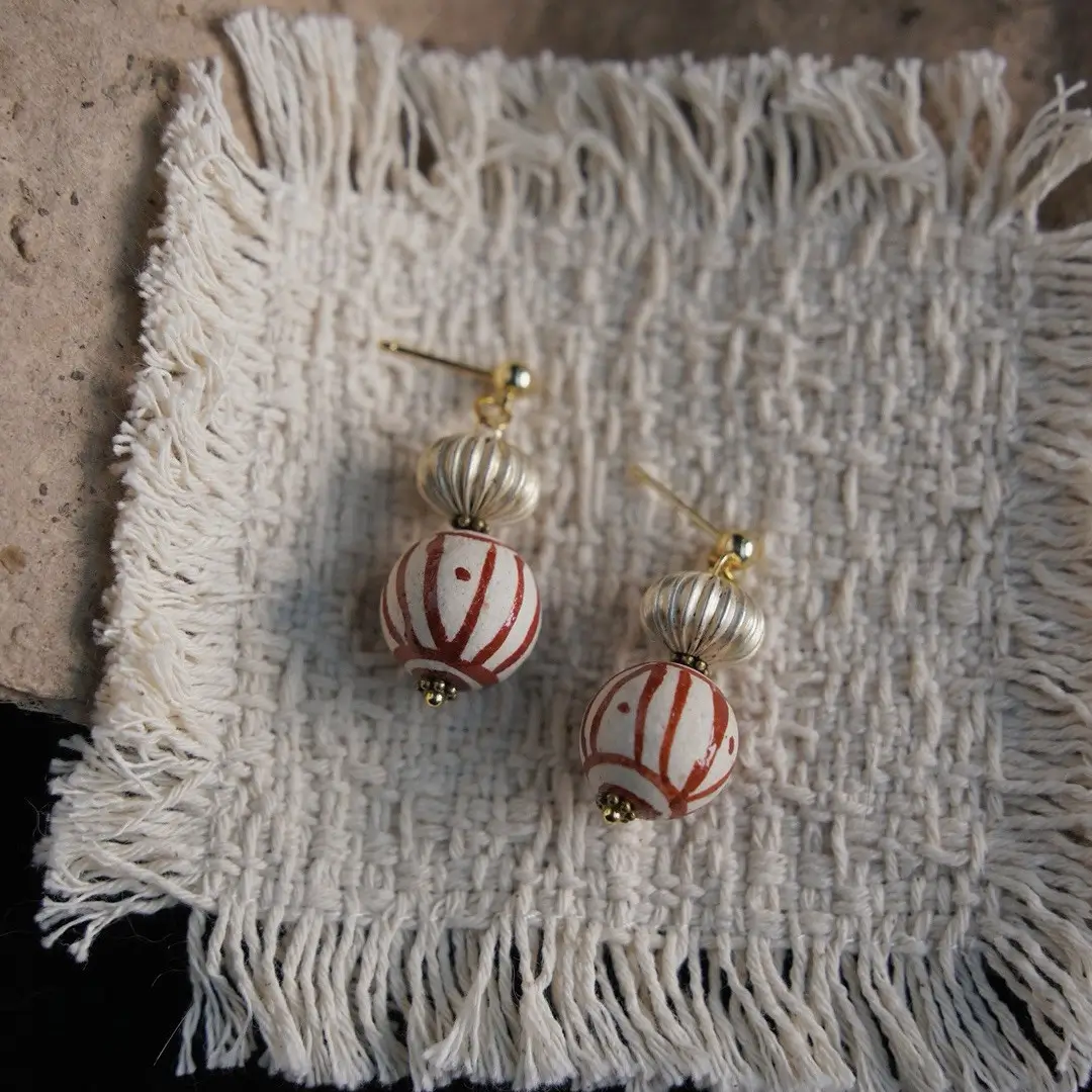 Vintage red striped glass earrings on white hand-woven fabric, flat lay.