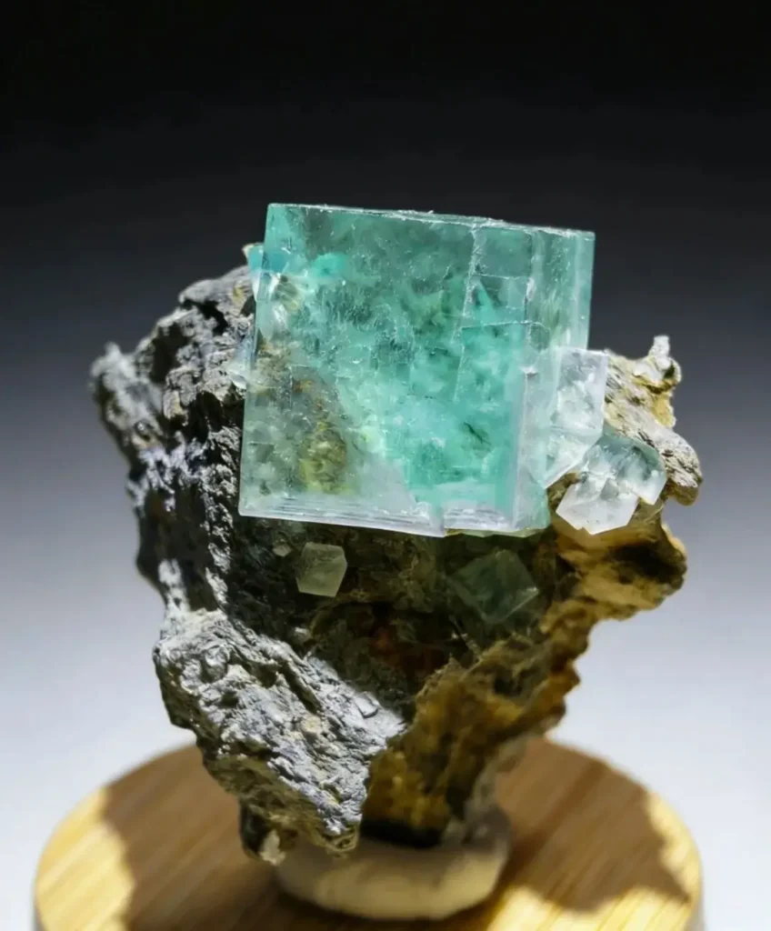 A sharp mint-green fluorite cube sitting on a dark rock matrix from Hunan.
