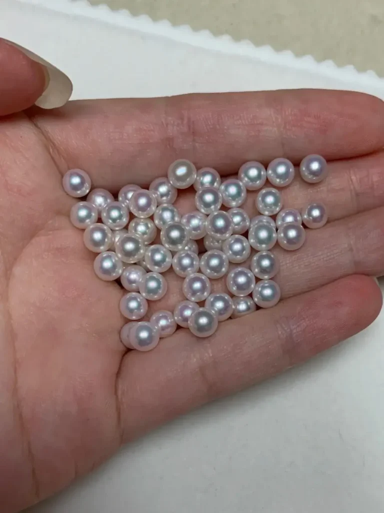A handful of small, perfectly round white freshwater pearls showing a sharp, pinkish-blue luster.