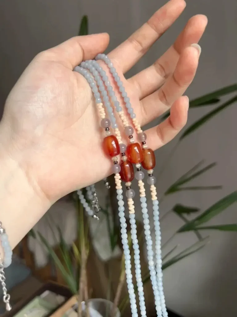 Hand holding multiple light blue chalcedony necklaces with central red carnelian accents.