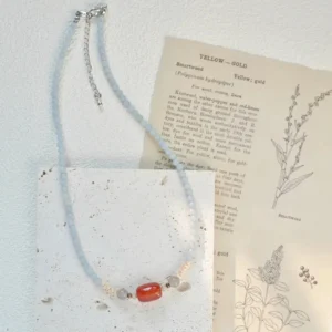 Minimalist blue chalcedony beaded necklace with a central red agate stone on a white stone tile.