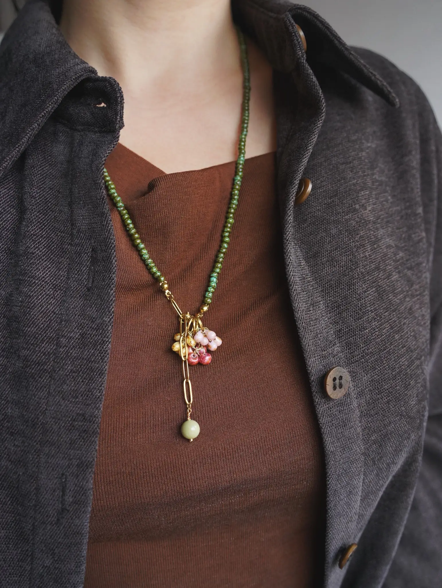 A model styling a botanical beaded Y necklace with an open dark grey jacket over a brown top.